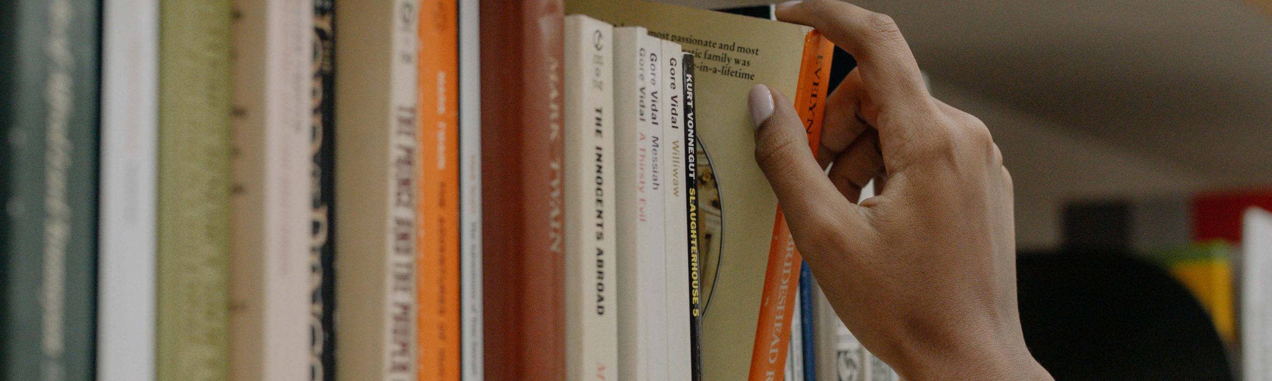 A hand reaching out to grab a book from a shelf filled with various titles.